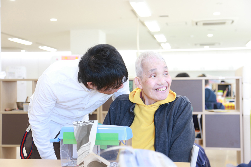 室内で施設の方が素敵な笑顔をしている利用者さんに話しかけている様子。